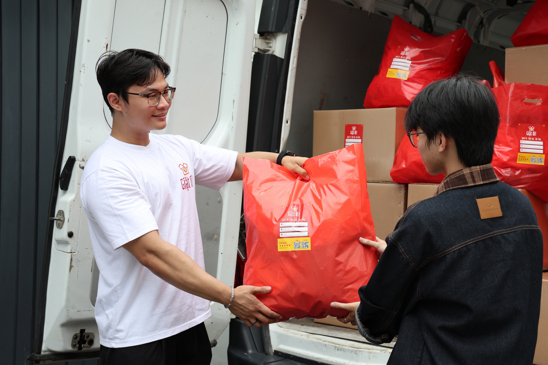 A Giặt Ơi! team member hands a bag of clean laundry to a customer